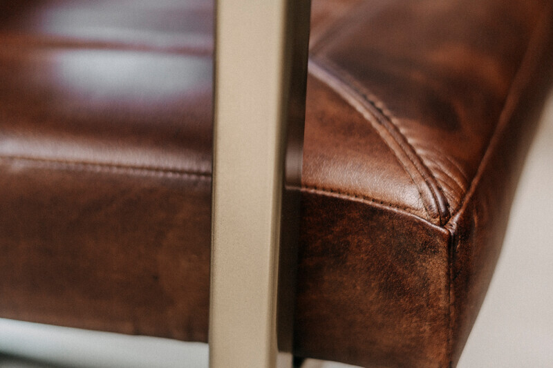 Makroaufnahme des hochwertigen braunen Leders und des beige Stahlgestells an der Seite eines Design-Polsterstuhls